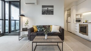 A modern living room with a sofa, coffee table, and a cityscape artwork. - Trendy Melbourne 2 Bedroom Apartment by BnB Pro (Melbourne)