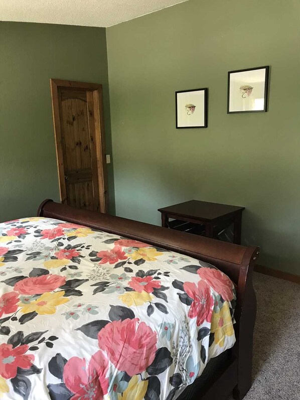 Un dormitorio con cubrecama floral, una puerta de madera y dos cuadros en la pared.