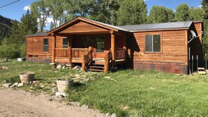 A wooden cabin with a porch, a satellite dish, and a metal roof. - Redcloud Getaway - Great Property Along the Lake Fork of the Gunnison with Direct Access to Trails (Lake City)