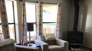 A living room with two armchairs, a coffee table, a fireplace, and a large window with curtains. - Redcloud Getaway - Great Property Along the Lake Fork of the Gunnison with Direct Access to Trails (Lake City)