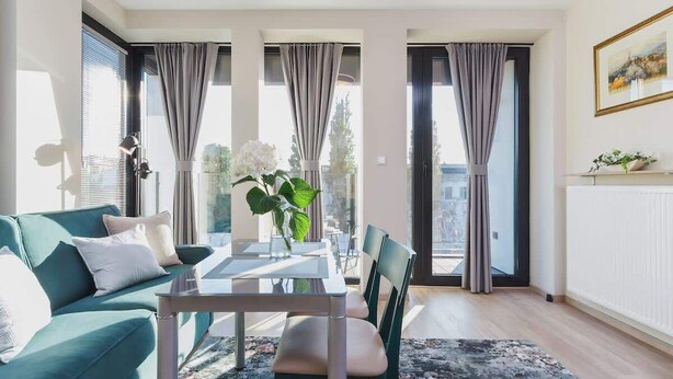 Een moderne woonkamer met een blauwgroene bank, een glazen eettafel en uitzicht door grote ramen.