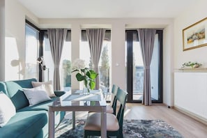 Un salon moderne avec un canapé de couleur turquoise, une table à manger en verre et une vue dégagée grâce à de grandes fenêtres.