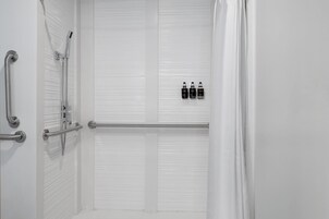 A white bathroom with a shower, grab bars, and three bottles of shampoo on the wall.