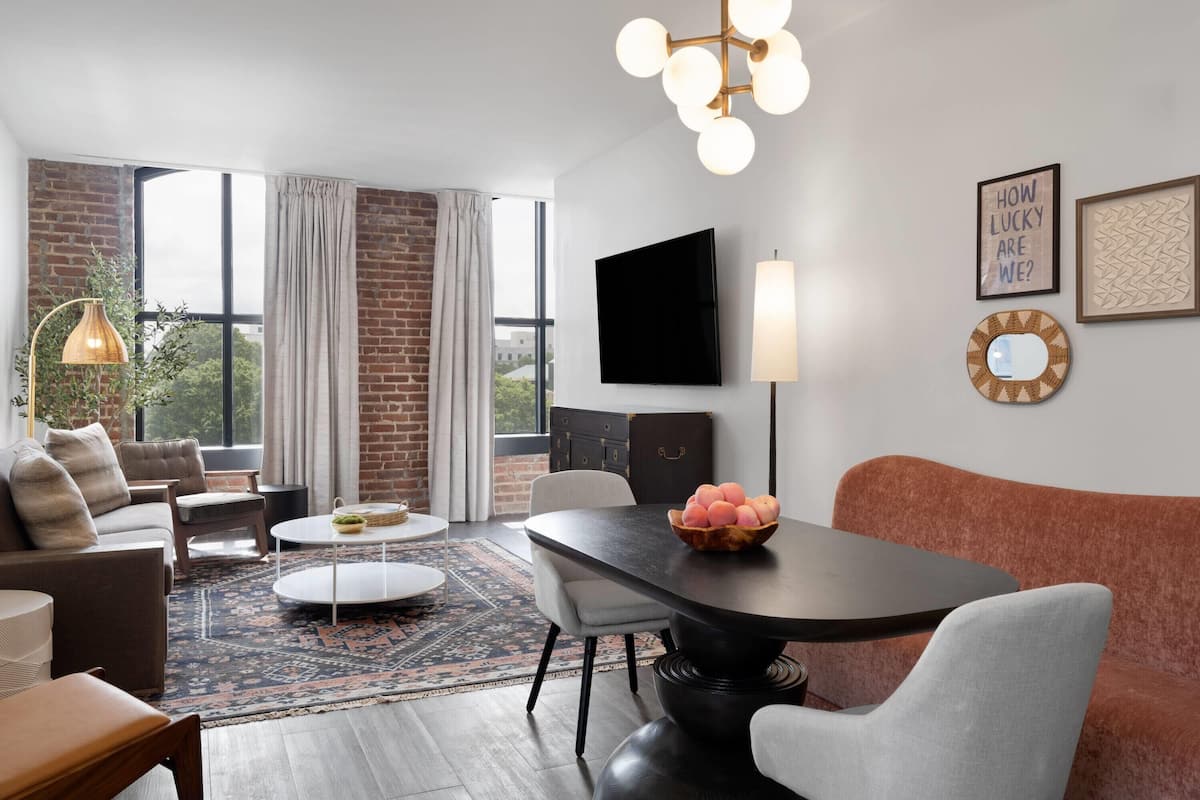 A modern living room with a sofa, chairs, a coffee table, a dining table, and a TV mounted on the wall.