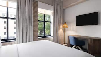 Une chambre d’hôtel avec un grand lit, un bureau avec une chaise, un téléviseur fixé au mur et une fenêtre avec des rideaux.