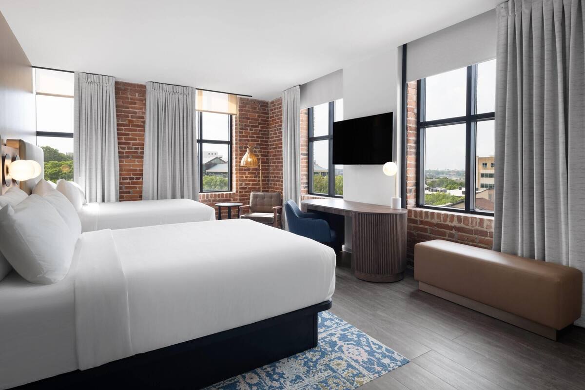 A hotel room with a large bed, a desk, a chair, a bench, and a TV.