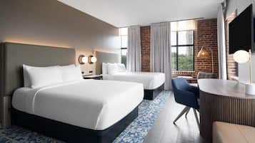A hotel room with a large bed, two smaller beds, a desk, and a chair. There are curtains, a TV, and a lamp.