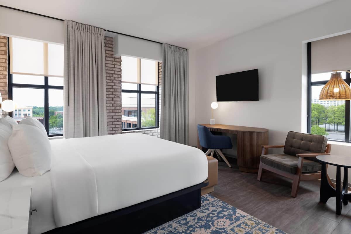 A modern hotel room with a large bed, a desk, a chair, and a TV on the wall.