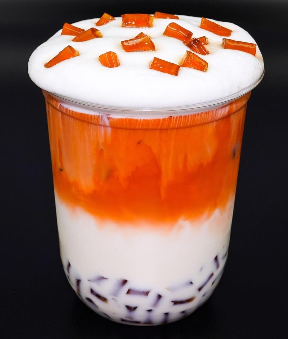 Un dessert composé de plusieurs couches, présenté dans un verre transparent, avec des couches orange et blanches et des morceaux de caramel sur le dessus.