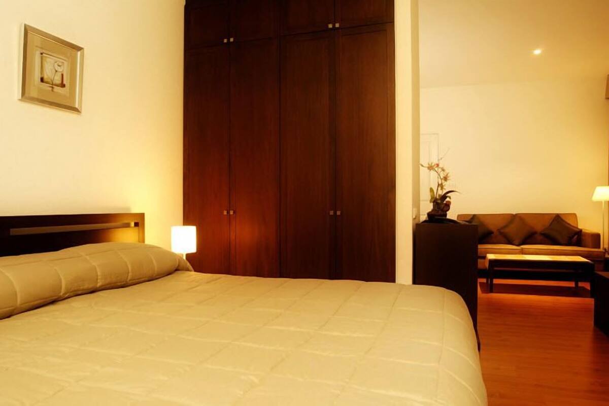 Hotellihuone, jossa on sänky, puinen vaatekaappi, sohva ja pieni pöytä.