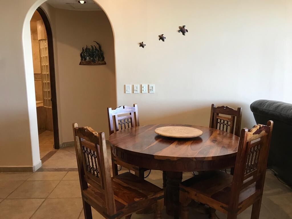 A round wooden dining table with chairs, a white plate, and wall-mounted light switches.