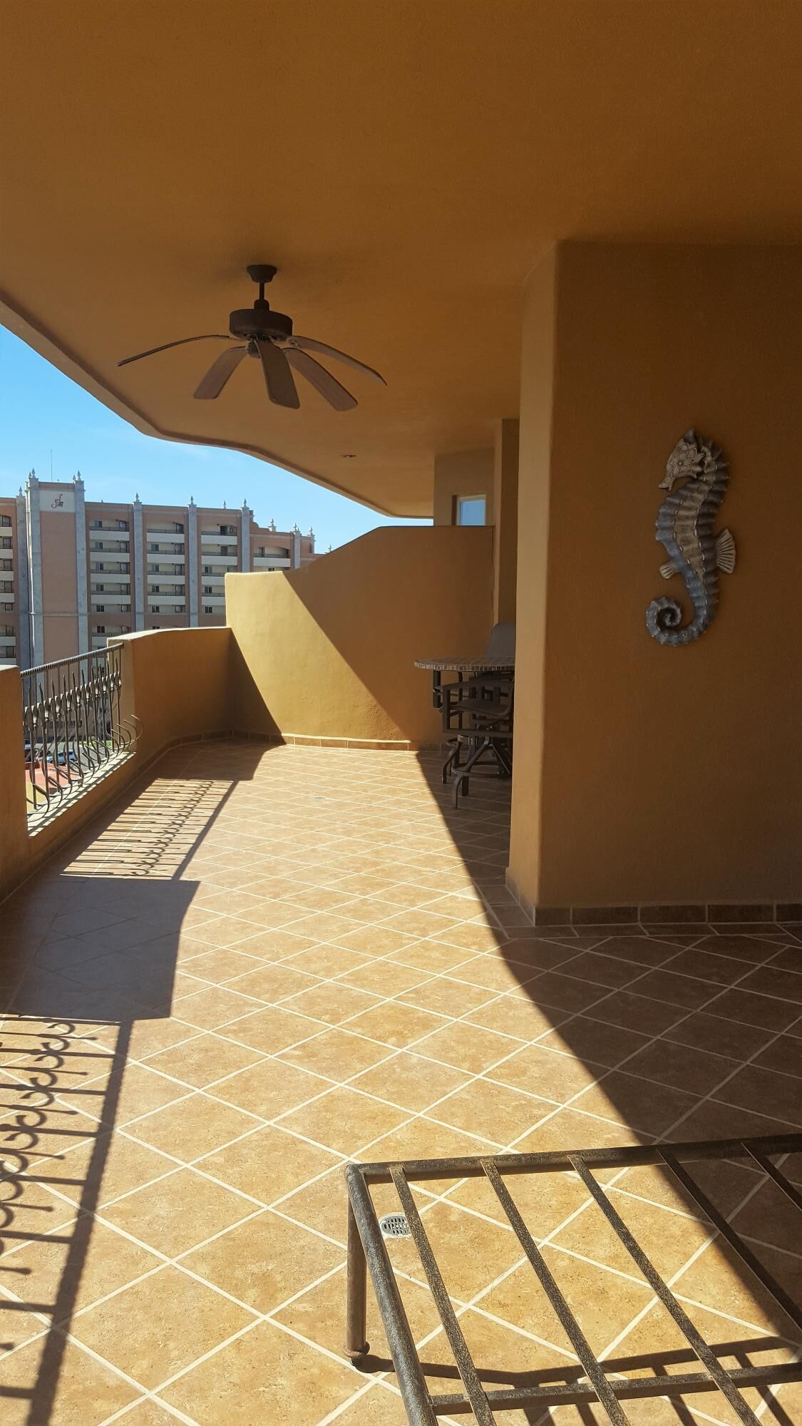 A sunlit balcony with a ceiling fan, tiled floor, and a decorative seahorse.