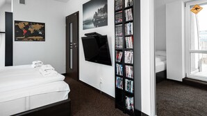 A hotel room with a bed, a wall-mounted TV, a bookshelf, a world map, and a window with a view.