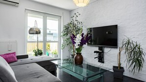 A modern living room with a sofa, a glass coffee table, a flat-screen TV mounted on a white brick wall, and a potted plant.