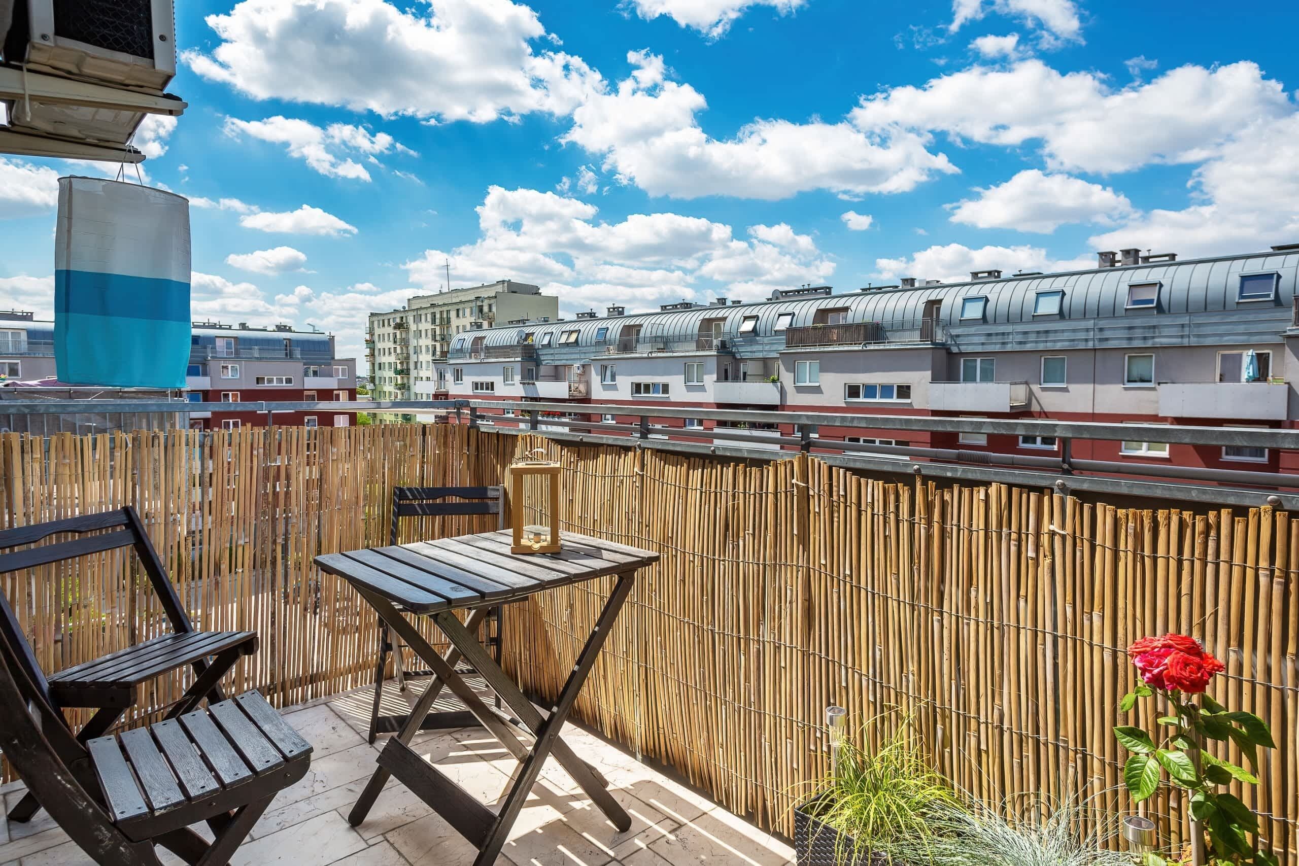 Un balcon avec une table et des chaises, une clôture en bambou et une rose rouge.