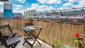 A balcony with a table and chairs, a bamboo fence, and a red rose.