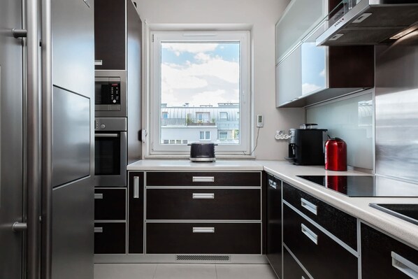 A modern kitchen with a built-in oven, a window with a view of buildings, and a stainless steel refrigerator.