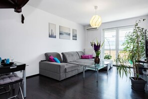 Een moderne woonkamer met een grijze bank, een glazen salontafel en een hanglamp.
