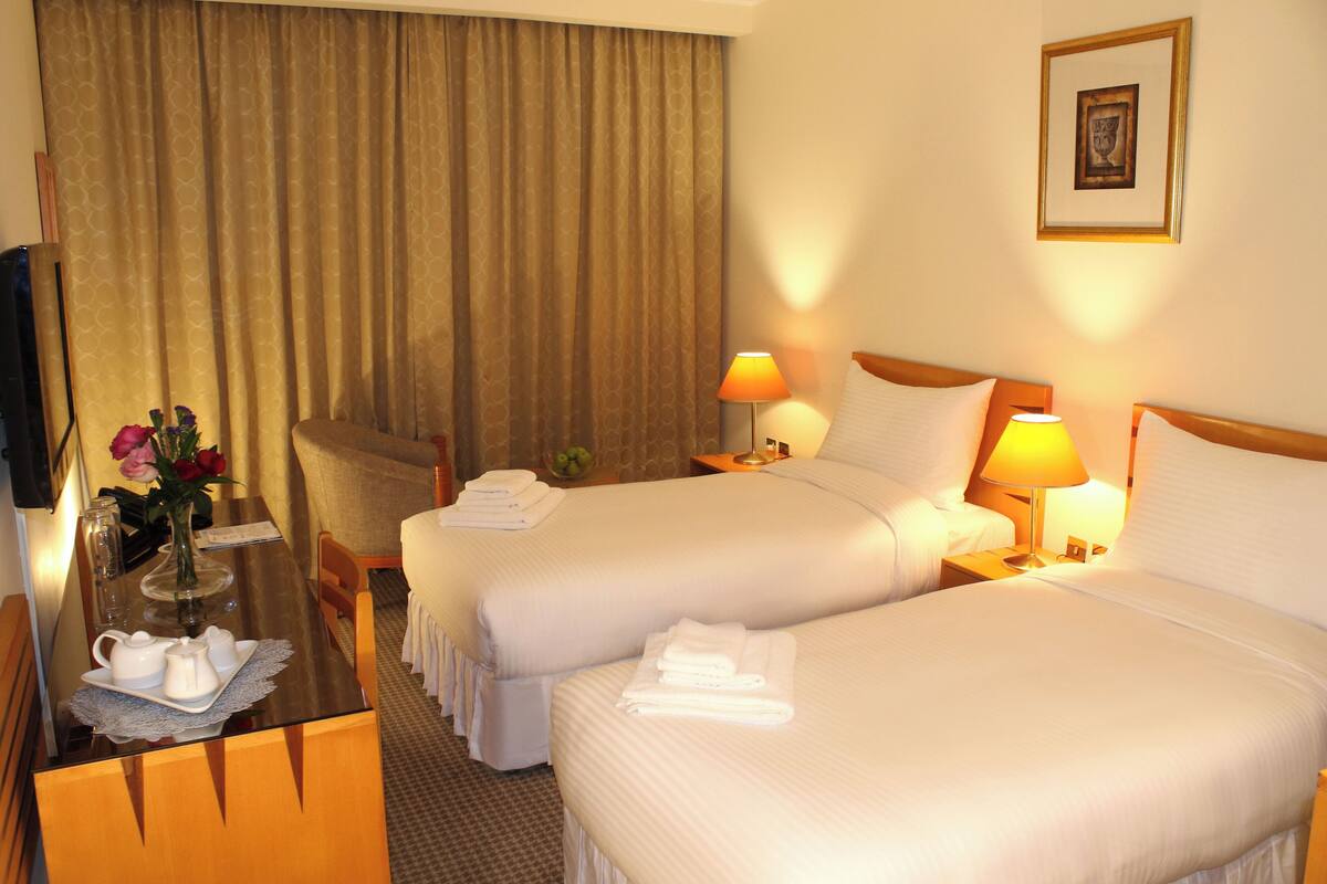 A hotel room with two beds, a desk with a vase of flowers, and a television.