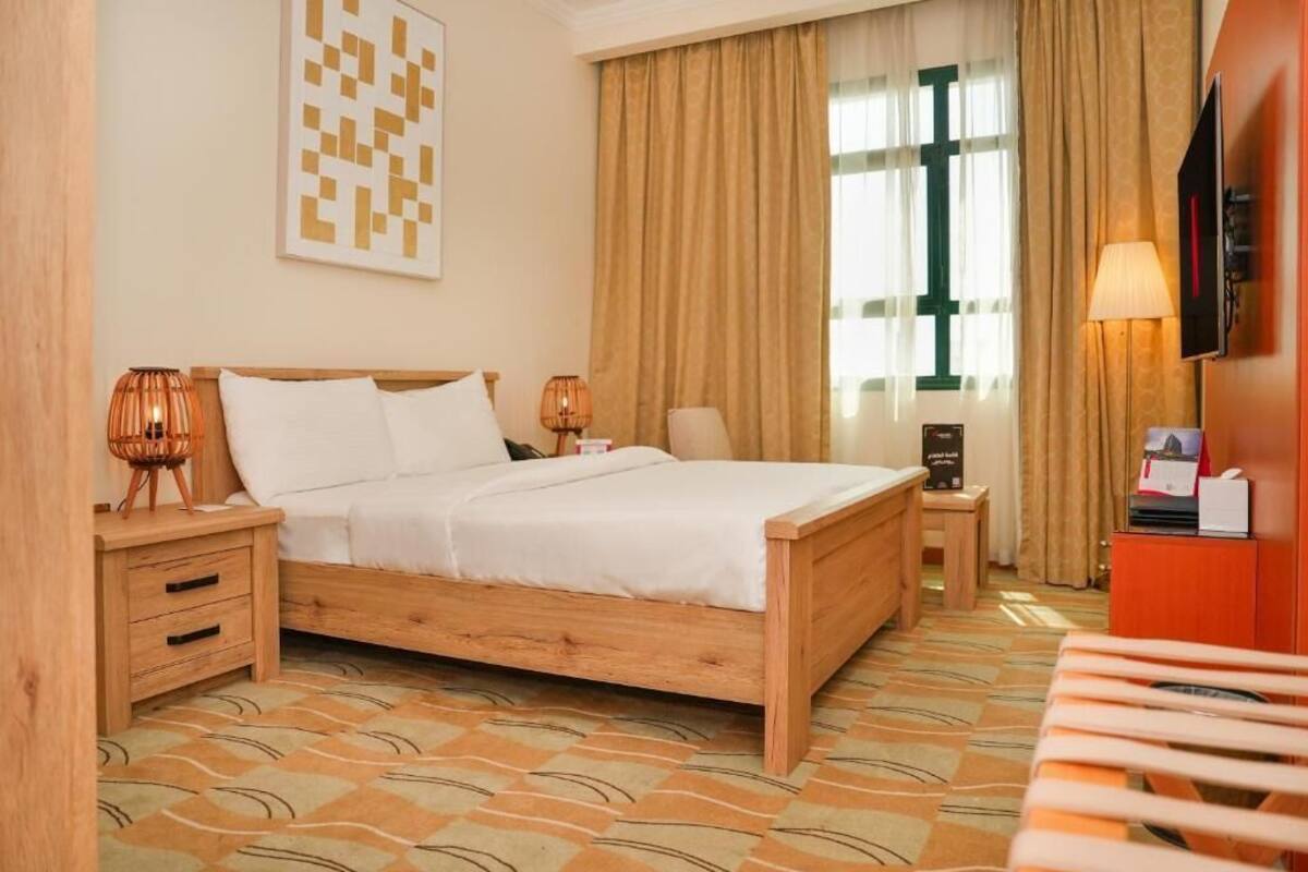 A hotel room with a wooden bed, two bedside tables, a TV, and a desk with a chair.