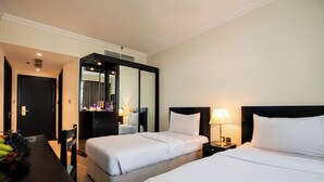 A hotel room with two beds, a desk with a fruit bowl, a mirror, and a nightstand with a lamp. - Swiss-Belinn Doha (Doha)