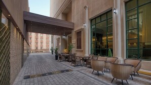 A covered outdoor seating area with wicker furniture and a tiled floor. - Swiss-Belinn Doha (Doha)