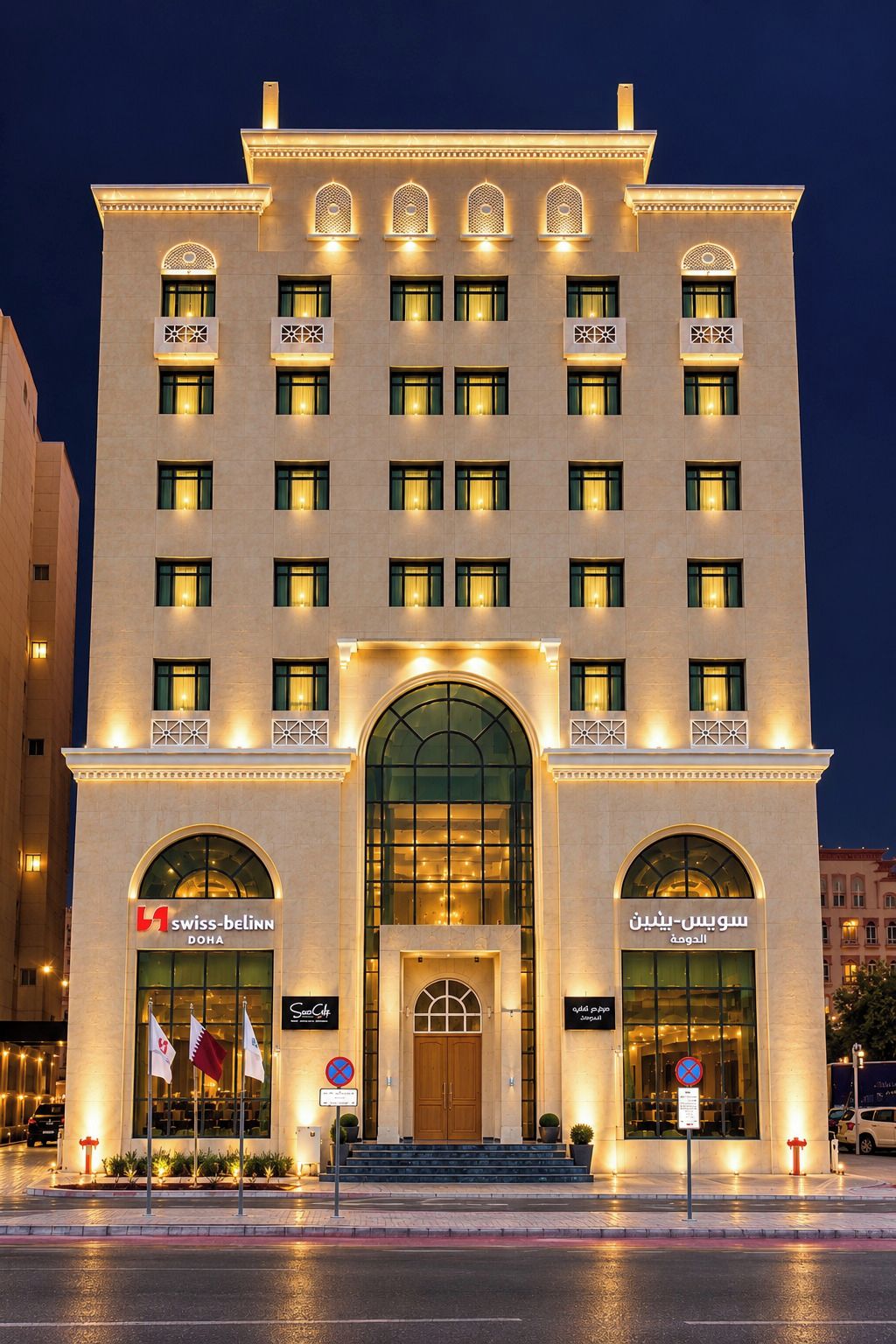 A hotel with multiple floors, large arched windows, and illuminated signage for Swiss-Bellinn Doha and Swoosh.