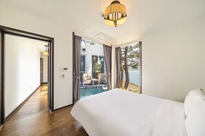 A hotel room with a large bed, a view of a pool and outdoor seating, and a ceiling light fixture. - Goseong Hansan Marina Resort (Goseong)