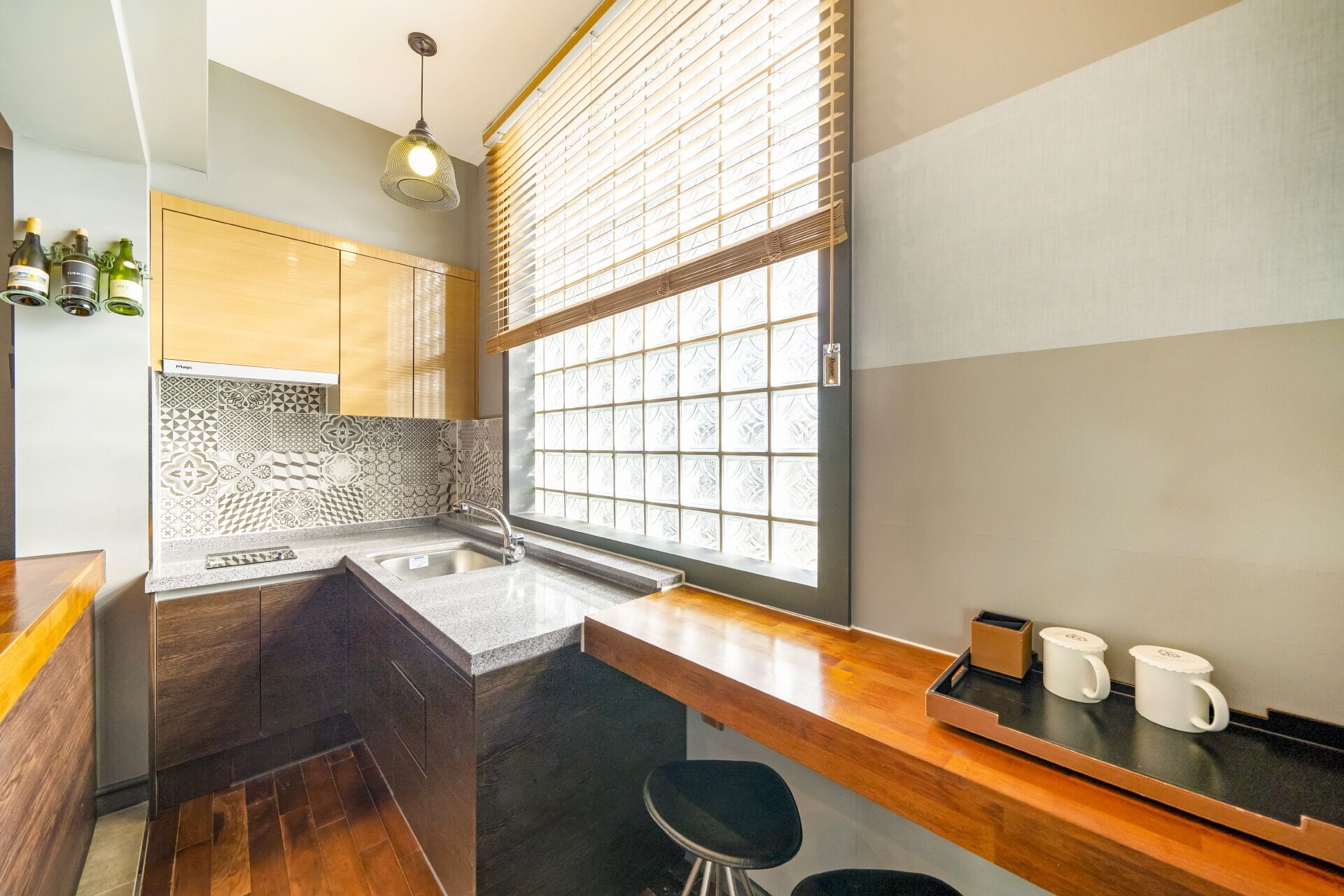 A modern kitchen with a built-in island, a large window with blinds, and a bar area with stools.