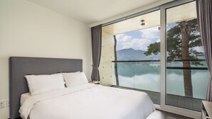 A bedroom with a large bed, a view of a lake, and a mountain in the background. - Goseong Hansan Marina Resort (Goseong)