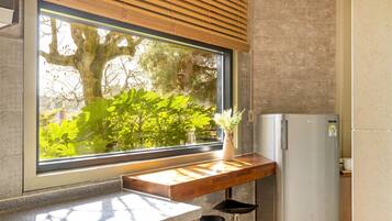 A kitchen with a large window, a wooden countertop, a white refrigerator, and a small stool.