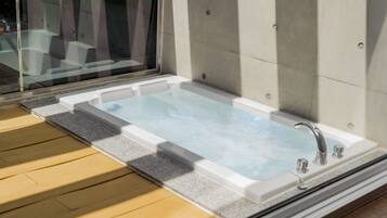 A rectangular hot tub with a glass top, positioned on a wooden deck adjacent to a glass window.