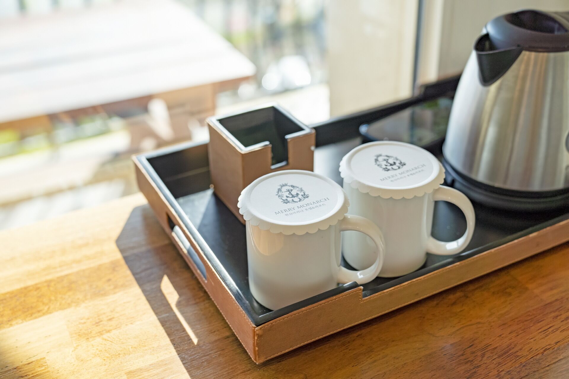 Una bandeja con dos tazas blancas y una cafetera plateada sobre una mesa de madera.