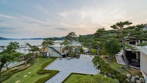 A modern building with a glass facade overlooking a body of water, surrounded by well-maintained gardens and trees. - Goseong Hansan Marina Resort (Goseong)