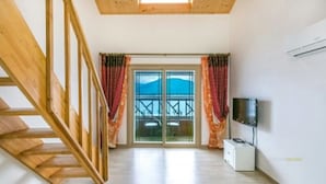 Una habitación con una escalera de madera, un ventanal corredero que da a un balcón y un televisor de pantalla plana en la pared.