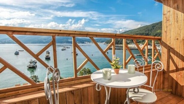Terraza de madera con mesa y sillas con vistas a un cuerpo de agua y barcos.
