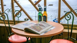 Una mesa con una revista y dos botellas, con vista a un cuerpo de agua con barcos.