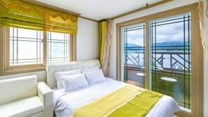 Una habitación de hotel con una cama, un sillón blanco y ventanas amplias con cortinas.