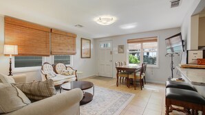 A living room with a sofa, a coffee table, a dining table with chairs, and a TV stand with a TV. - Quiet and safe Uptown house steps from Audubon Zoo and shopping on Magazine (New Orleans)