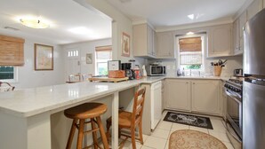 A kitchen with a white countertop, wooden stools, a microwave, a stove, and a refrigerator. - Quiet and safe Uptown house steps from Audubon Zoo and shopping on Magazine (New Orleans)