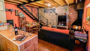 Una sala de estar acogedora con chimenea de piedra, vigas de madera, una escalera y un comedor con mesa y sillas.