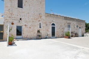 Il s’agit d’un bâtiment en pierre doté d’une grande porte d’entrée en arc de cercle, d’une petite fenêtre et d’une porte. On y trouve des plantes en pot et un banc en métal à l’extérieur.