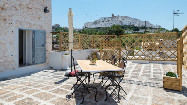 Eine Terrasse mit Tisch und Stühlen, einem Blumentopf und Blick auf eine Stadt auf einem Hügel.
