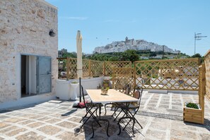 Une terrasse avec une table et des chaises, un pot de fleurs et une vue sur une ville perchée sur une colline.