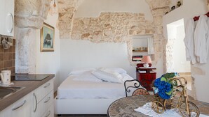 Ein Schlafzimmer mit Stewand, einem Bett, einem kleinen Tisch mit Korb und Blumen sowie einer Küchenzeile mit Spüle und Schränken.