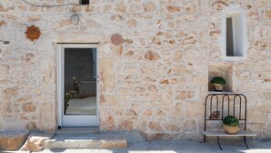 Ein Steinhaus mit einer Tür, einem kleinen Fenster und einer Bank mit Topfpflanzen.