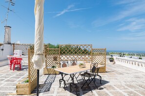 Une terrasse avec une table et des chaises, une chaise rouge, un parasol blanc et une vue sur la mer.