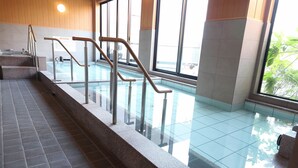 Una piscina interior con paredes de vidrio transparente, barandales de metal y suelo de baldosas.