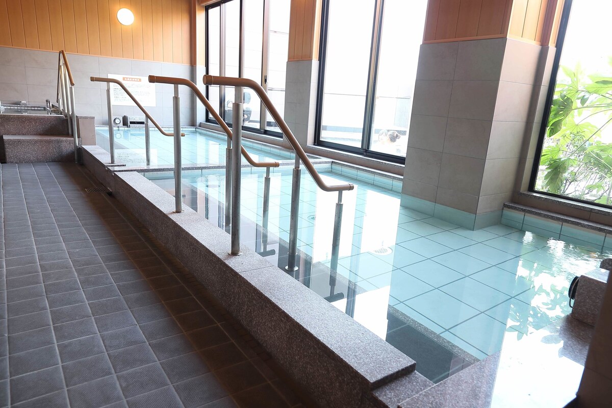 Une piscine intérieure avec des parois en verre transparent, des rampes métalliques et un revêtement de sol carrelé.