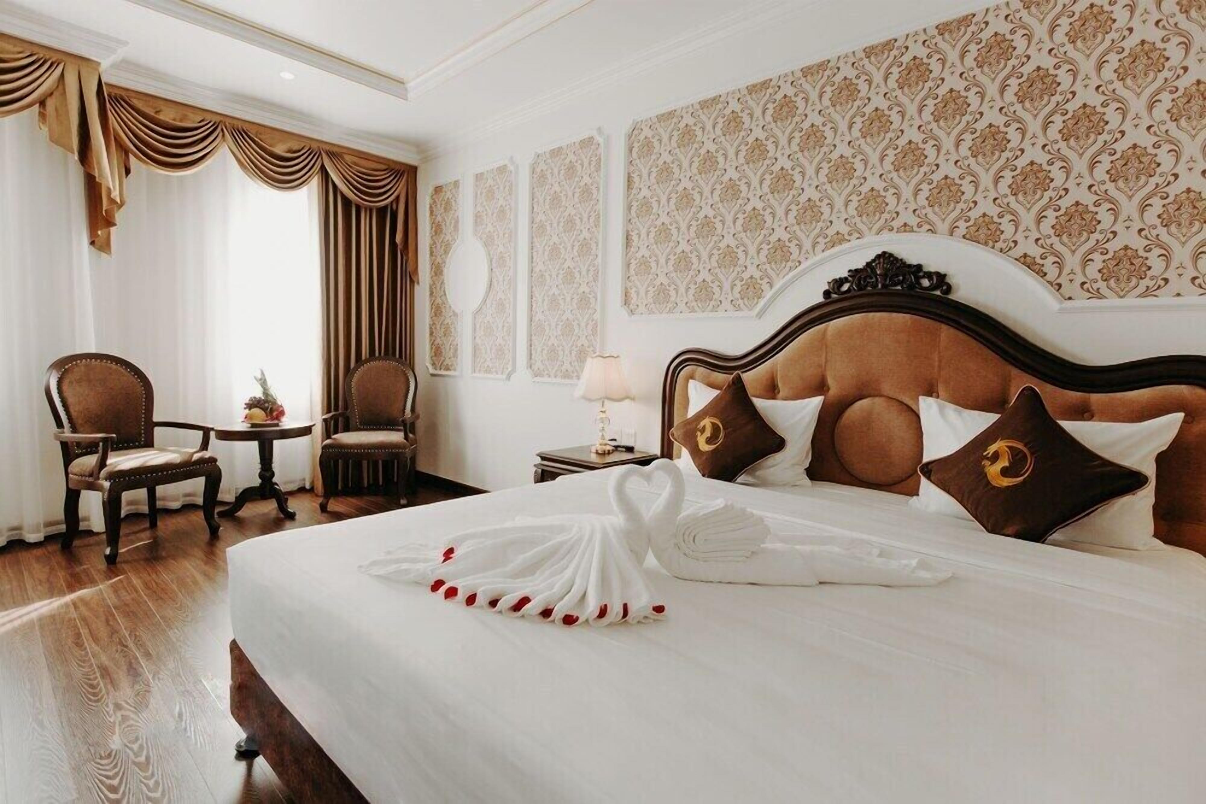 A hotel room with a large bed, two armchairs, a small table, and a lamp.